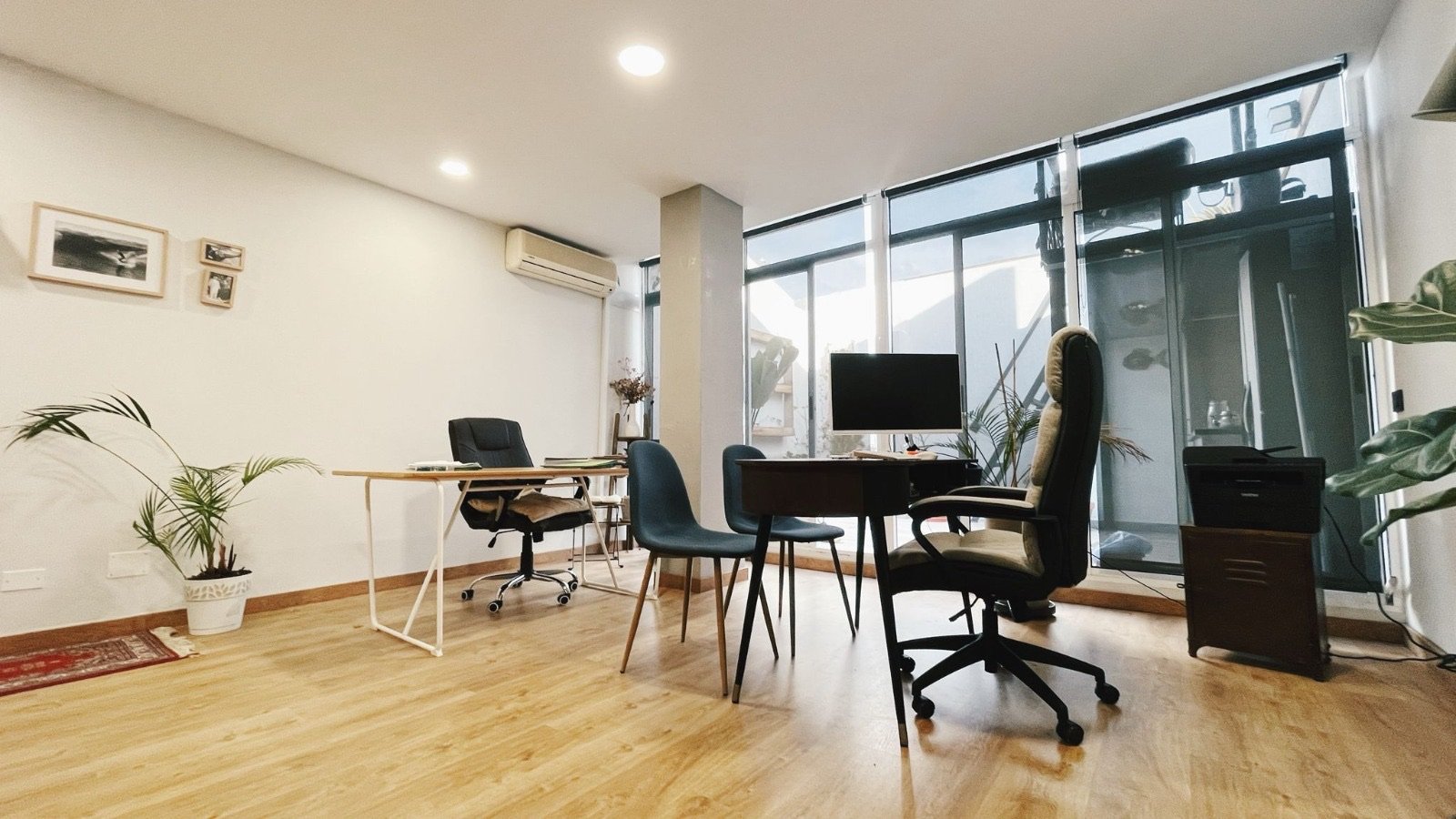Despacho de Sofía Compte: un espacio luminoso con grandes ventanales, suelo de madera, plantas y una mesa de reuniones.